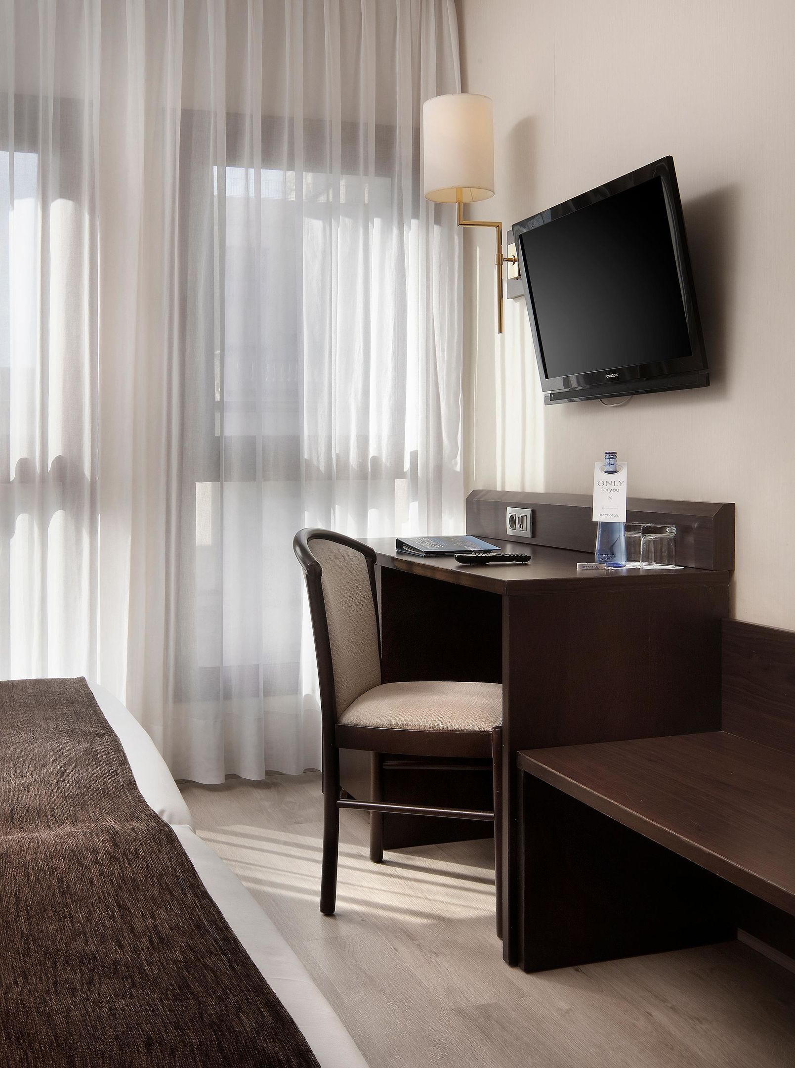 Una habitación de hotel con cama, escritorio, silla, televisión y lámpara.