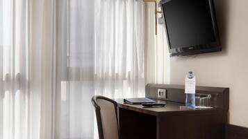 Una habitación de hotel con cama, escritorio, silla, televisión y lámpara.
