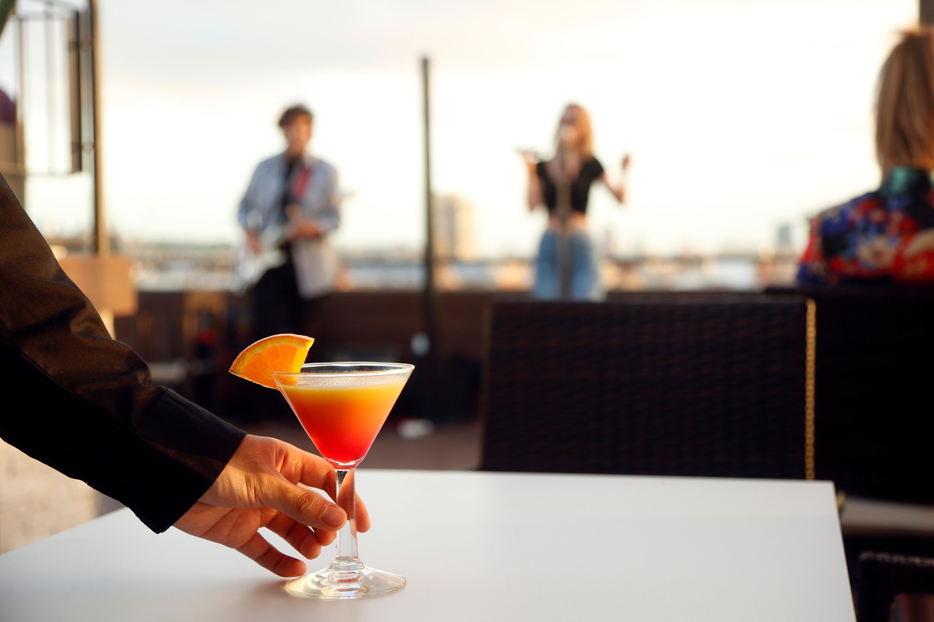 A person holding a cocktail glass with an orange garnish on a rooftop bar.