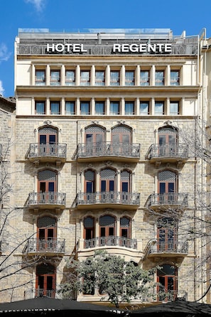 Un hotel de diverses plantes amb balcons, un rètol que diu “HOTEL REGENTE” i un cel blau clar al fons.