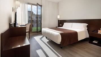 Habitación de hotel con cama, escritorio, silla, mesita de noche y vistas al exterior.