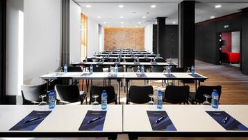 Un salón de conferencias con filas de mesas, sillas, botellas de agua y bolígrafos.