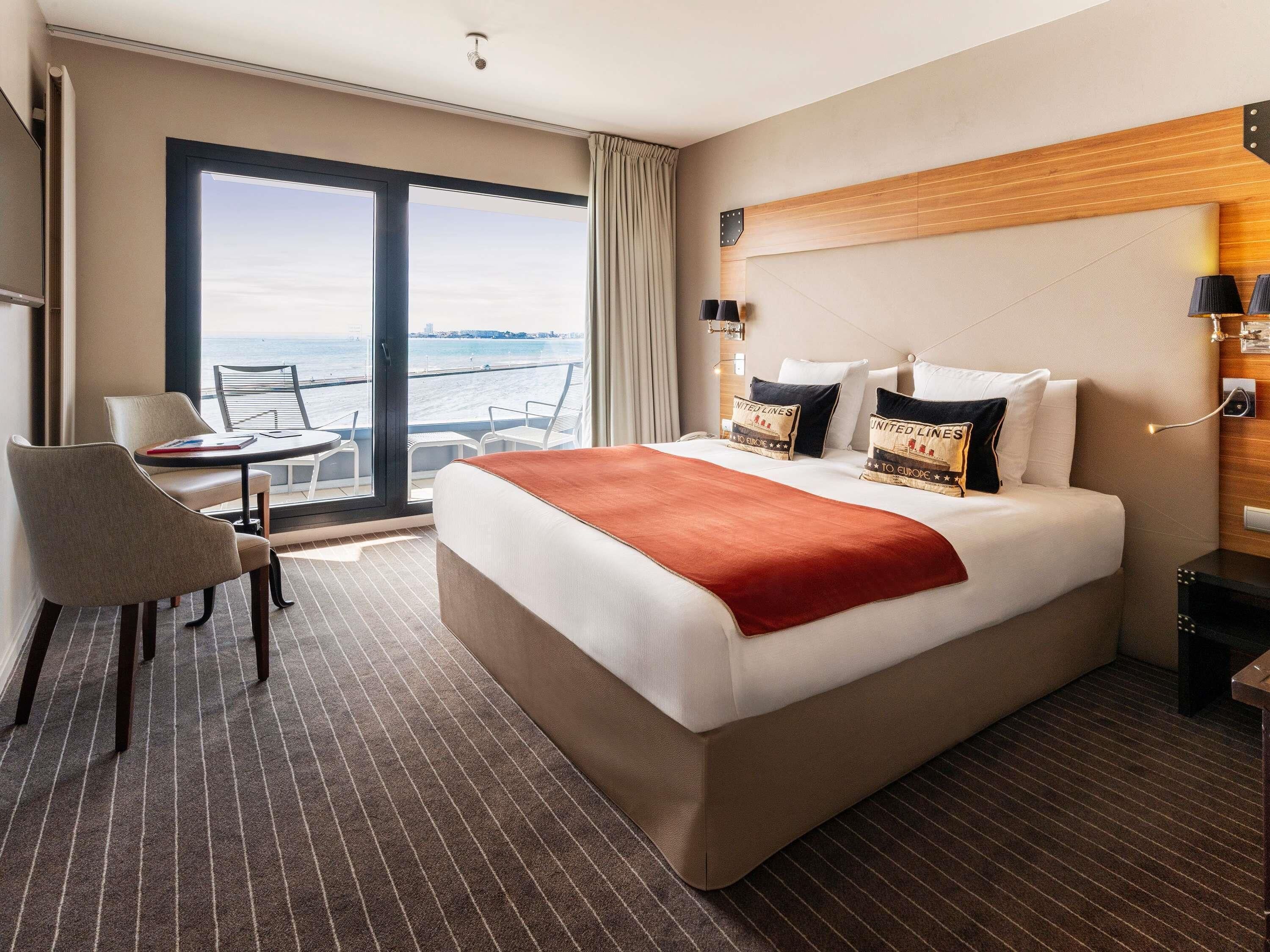 A hotel room with a large bed, a desk, and a chair.