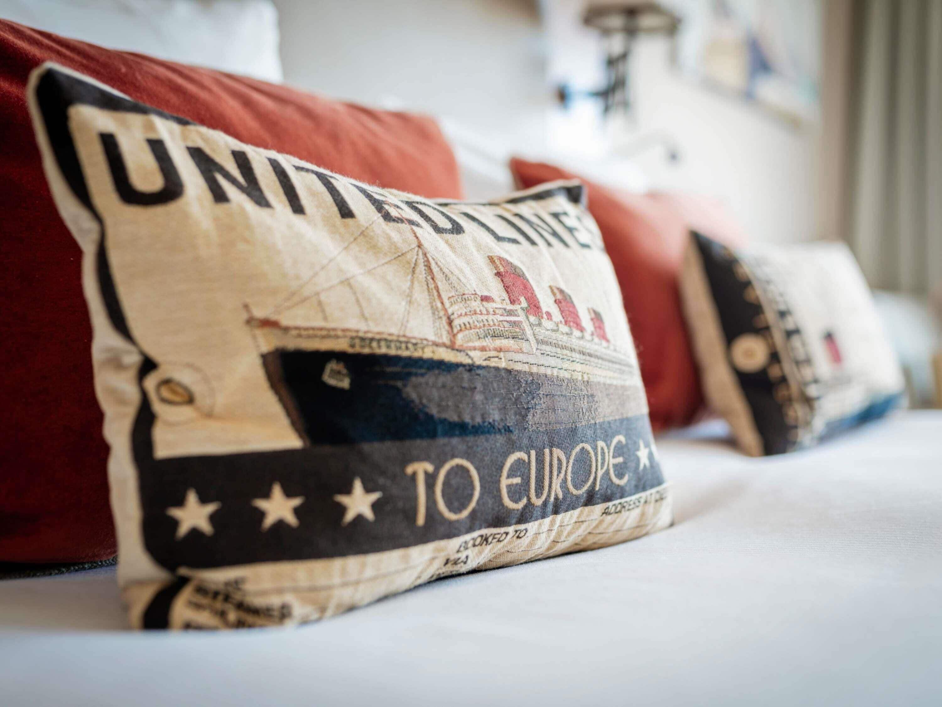 En pude med et vintage design, der viser et skib og teksten "UNITED STATES TO EUROPE".