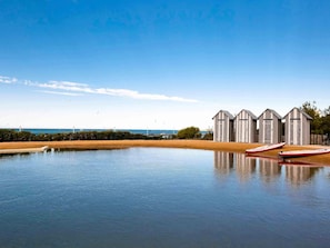 A calm body of water with boats, a sandy beach, and wooden structures in the background. - Côte Ouest Thalasso & Spa Les Sables d'Olonne - MGallery Collection (Les Sables-d'Olonne)