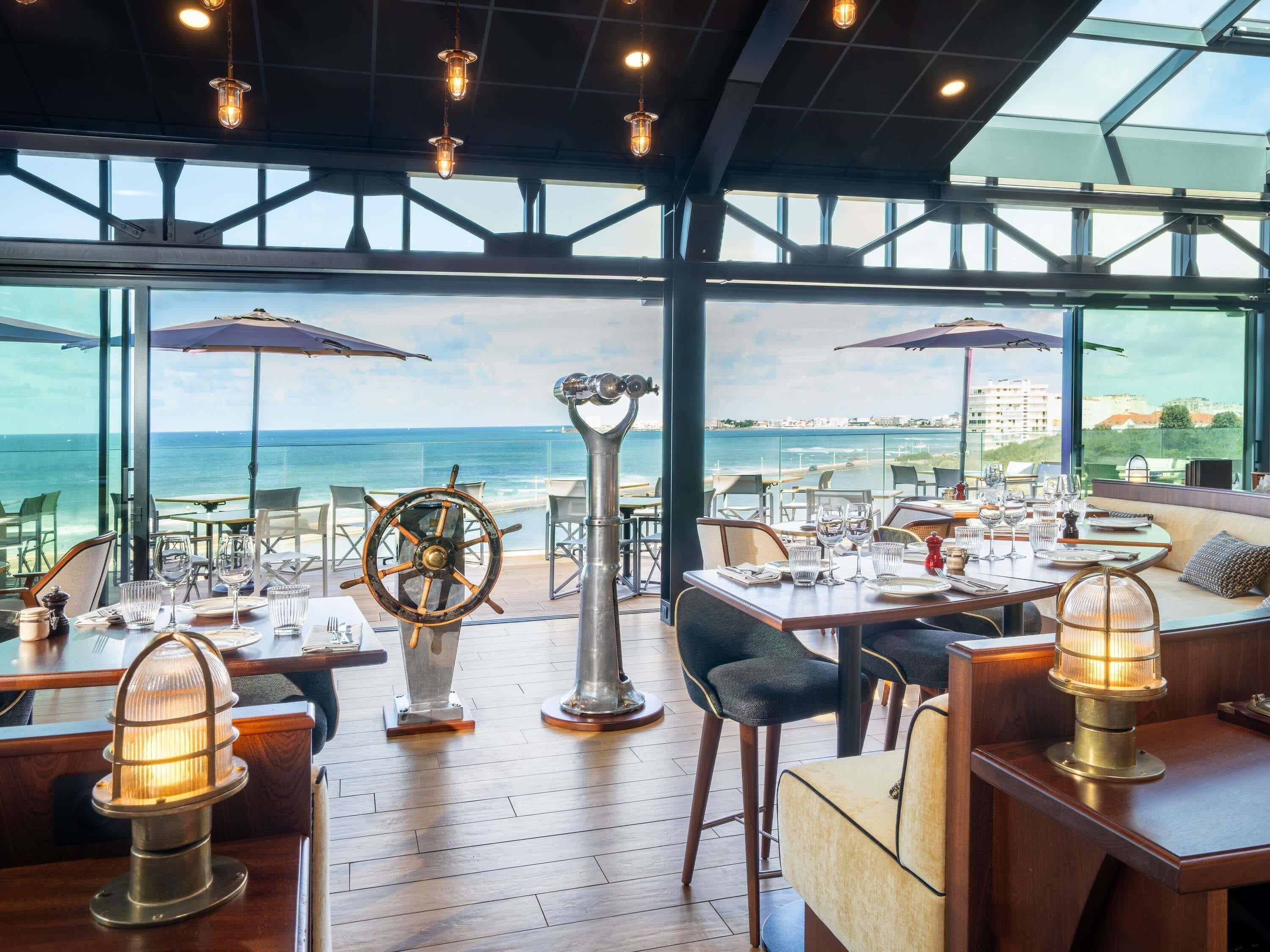 Un restaurant avec des tables, des chaises, un gouvernail de bateau et une vue sur la mer.