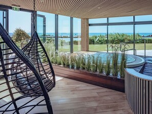 A modern indoor pool area with a view of the sea, a wooden ceiling, and a hanging chair. - Côte Ouest Thalasso & Spa Les Sables d'Olonne - MGallery Collection (Les Sables-d'Olonne)