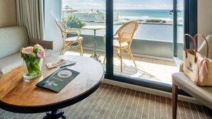 A hotel room with a balcony, a round table, wicker chairs, a sofa, and a view of the sea. - Côte Ouest Thalasso & Spa Les Sables d'Olonne - MGallery Collection (Les Sables-d'Olonne)