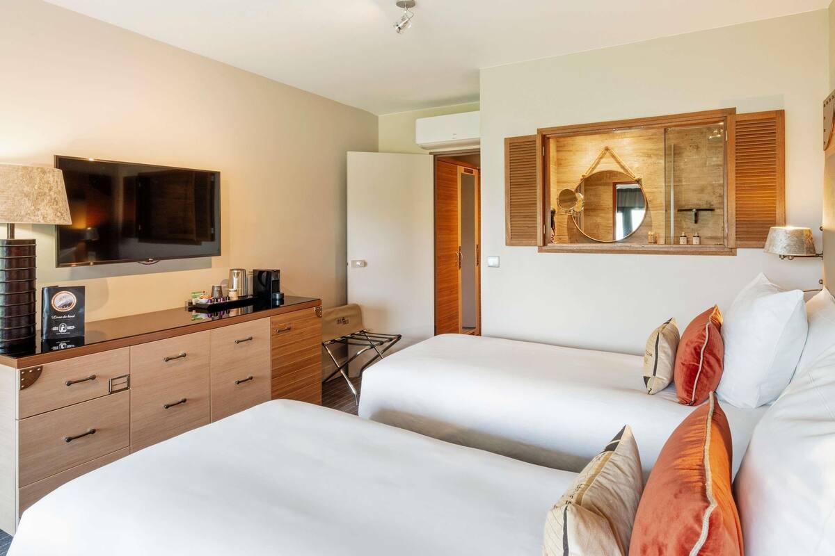 Une chambre d’hôtel avec deux lits, une télévision, une machine à café et une commode en bois.