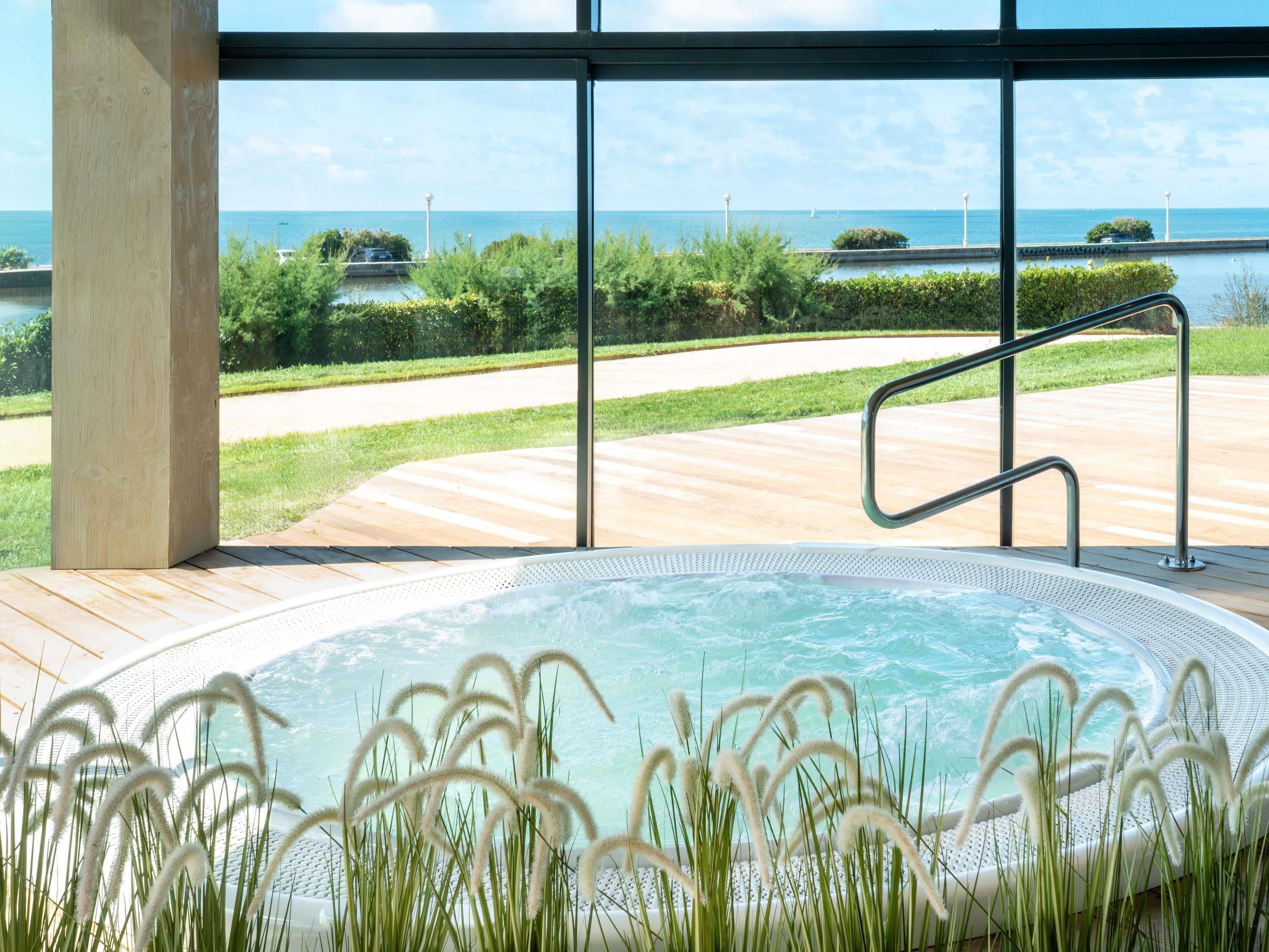 A hot tub with a view of the sea, surrounded by greenery and a wooden deck.