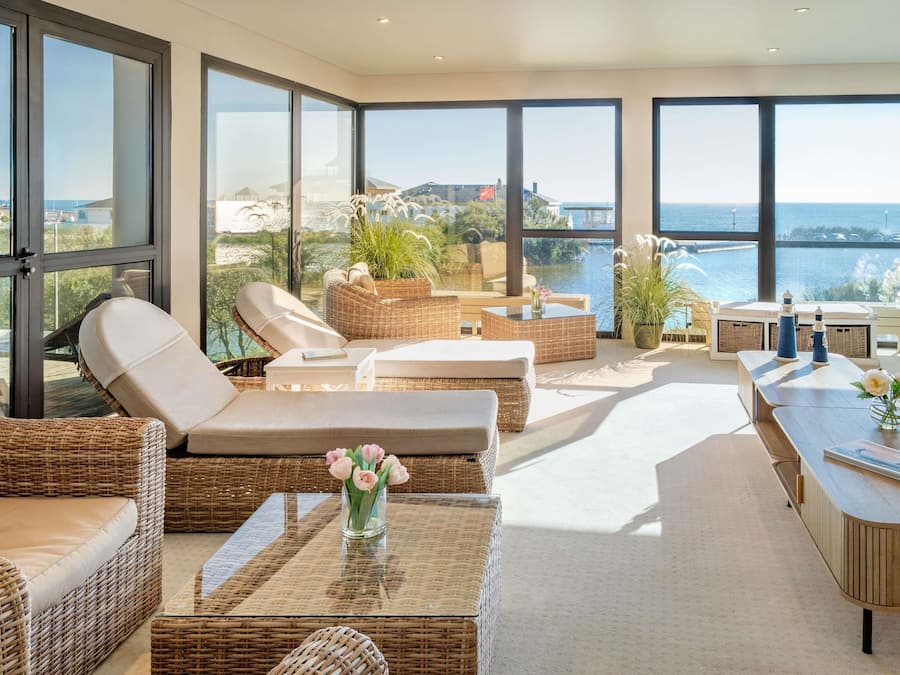 Un espace de détente moderne, avec des meubles en osier, une table basse en verre et une vue sur la mer.