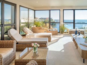 A modern lounge area with wicker furniture, a glass coffee table, and a view of the sea. - Côte Ouest Thalasso & Spa Les Sables d'Olonne - MGallery Collection (Les Sables-d'Olonne)