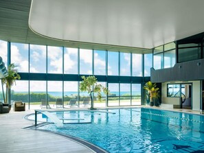 An indoor swimming pool with a view of the ocean, surrounded by large windows and furnished seating areas. - Côte Ouest Thalasso & Spa Les Sables d'Olonne - MGallery Collection (Les Sables-d'Olonne)