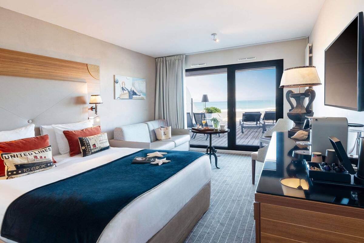 Une chambre d’hôtel équipée d’un lit, d’un bureau, d’un ordinateur portable, d’une machine à café et offrant une vue sur la plage.
