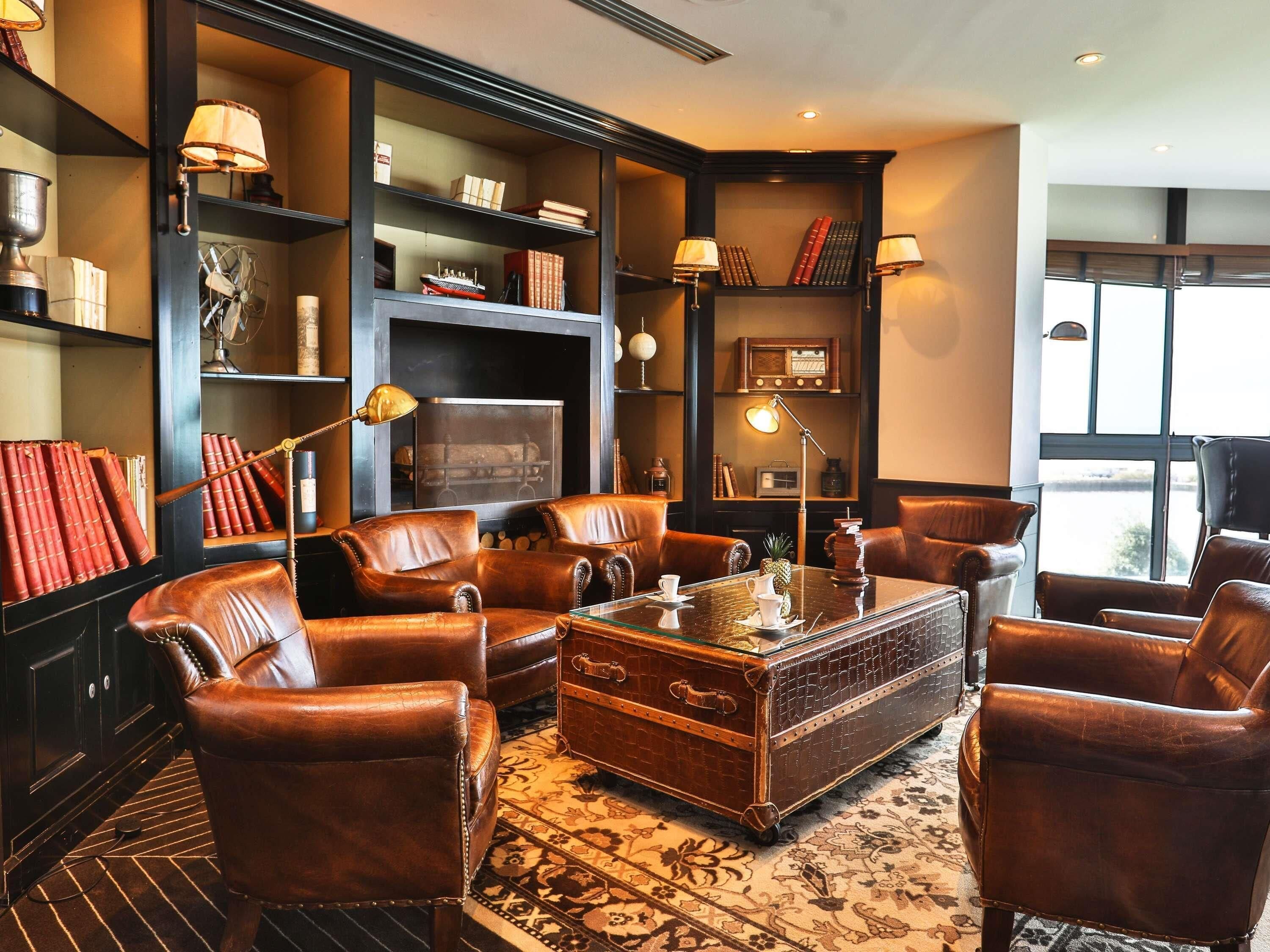 A cozy living room with leather furniture, a vintage trunk coffee table, and bookshelves filled with books and decorative items.