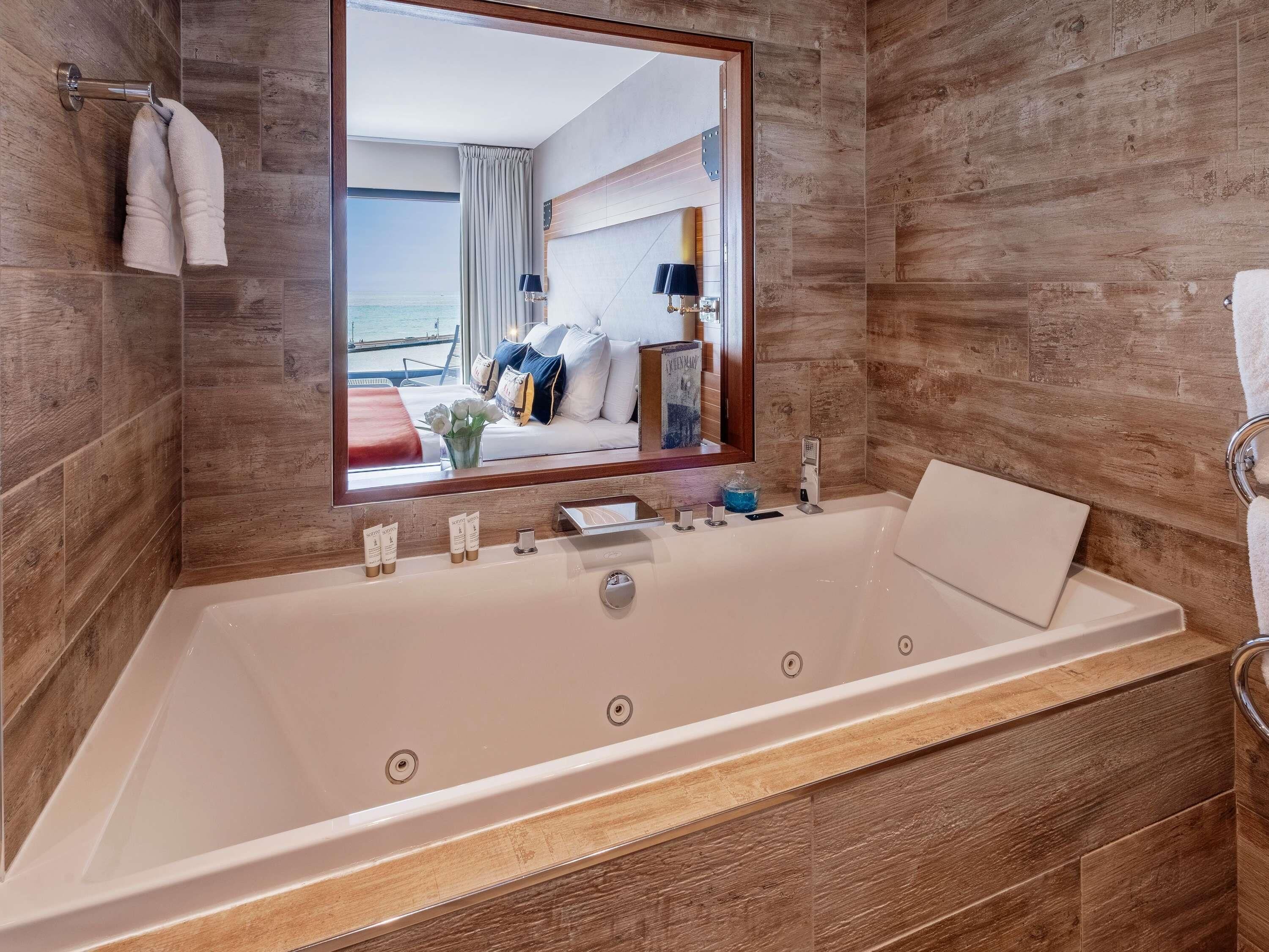 Un baño moderno con una bañera grande, un espejo y vistas a una habitación con cama y ventana.