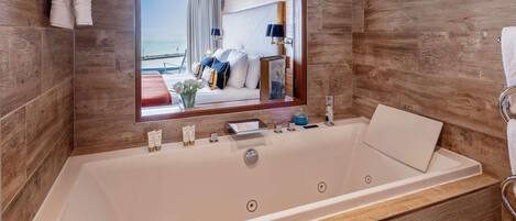 Un baño moderno con una bañera grande, un espejo y vistas a una habitación con cama y ventana.