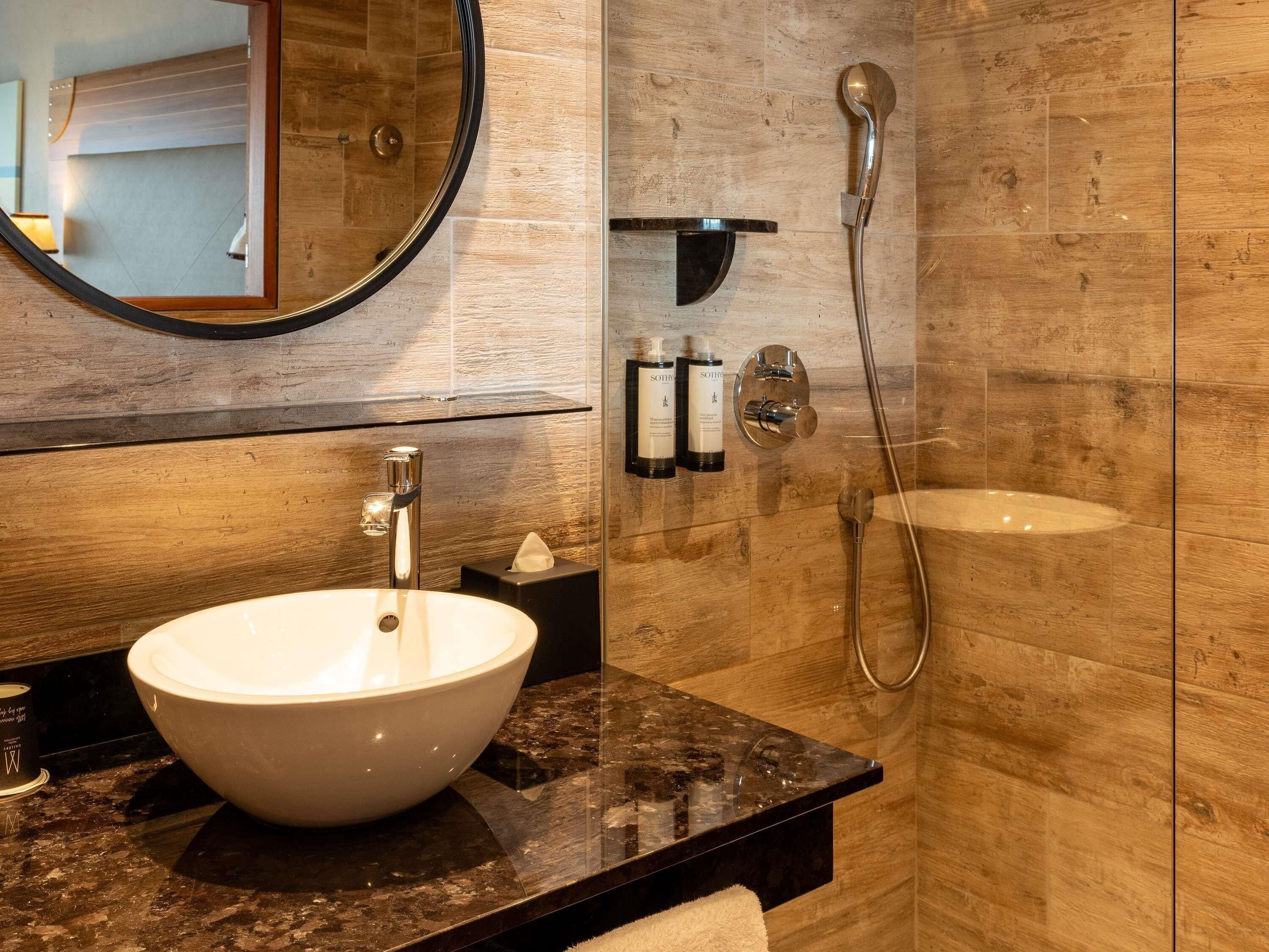 Une salle de bain moderne avec un grand lavabo blanc, un miroir, une douchette à main et un porte-serviettes.
