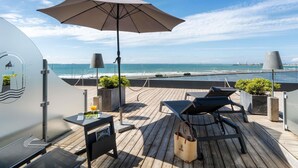 A wooden deck with lounge chairs, a table, and an umbrella overlooking a beach. - Côte Ouest Thalasso & Spa Les Sables d'Olonne - MGallery Collection (Les Sables-d'Olonne)