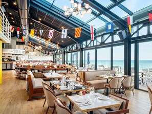 Ein Restaurant mit hohen Decken, großen Fenstern und Meerblick.