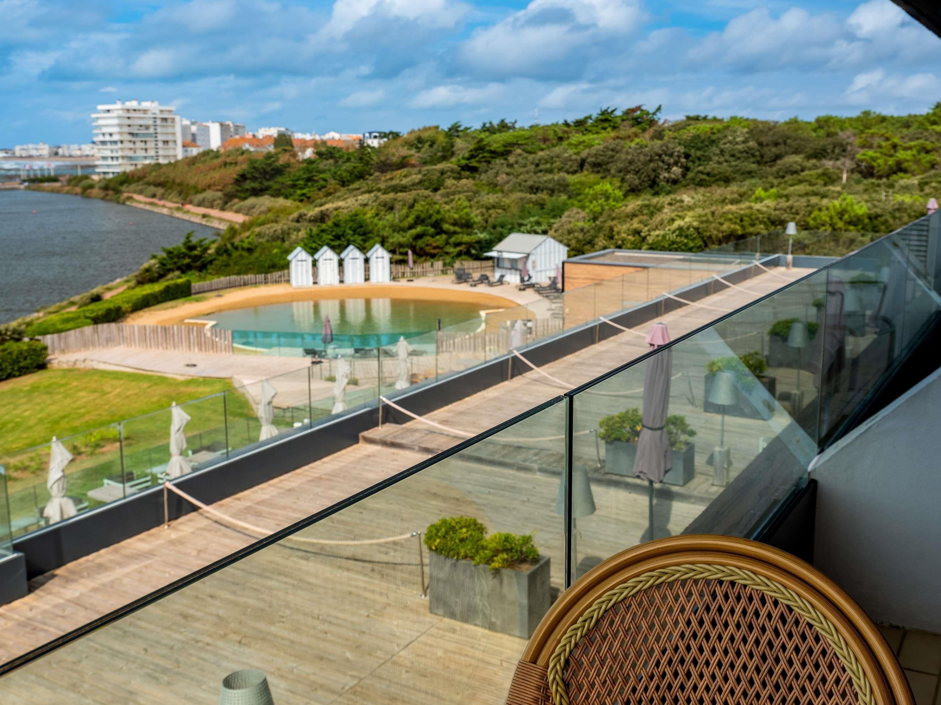 A glass balustrade overlooking a pool with a view of the sea and buildings in the background.