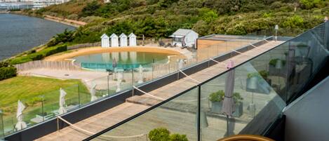 A glass balustrade overlooking a pool with a view of the sea and buildings in the background.
