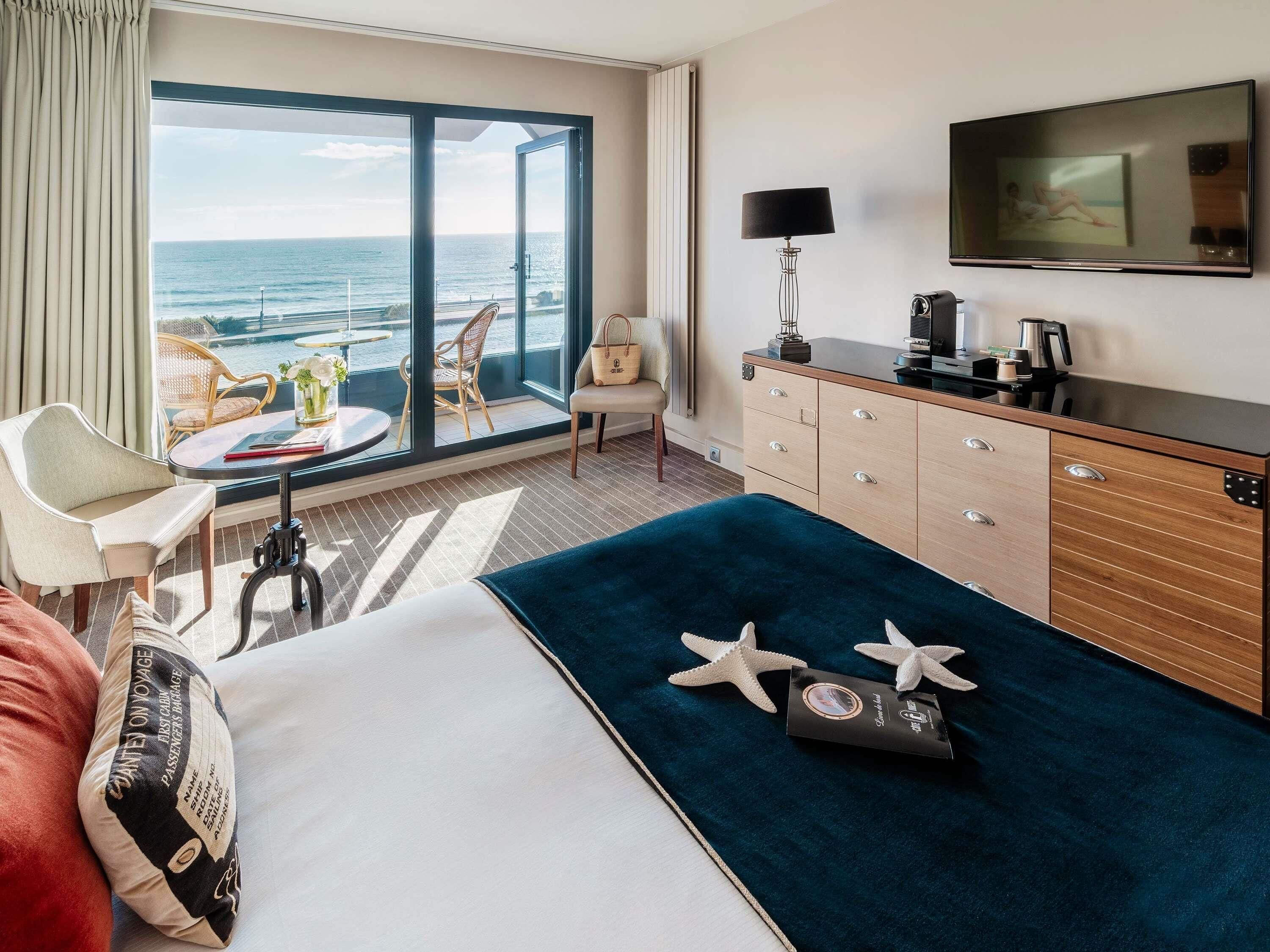 Habitación de hotel con cama, escritorio, silla, televisión y vista al océano.
