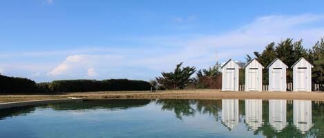 A clear pool with wooden deck, surrounded by three white sheds.