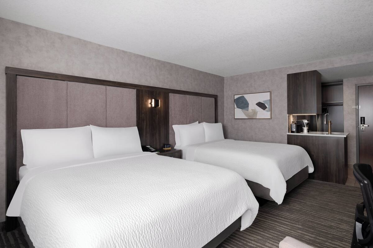 A hotel room with two beds, a small kitchenette, and a seating area.