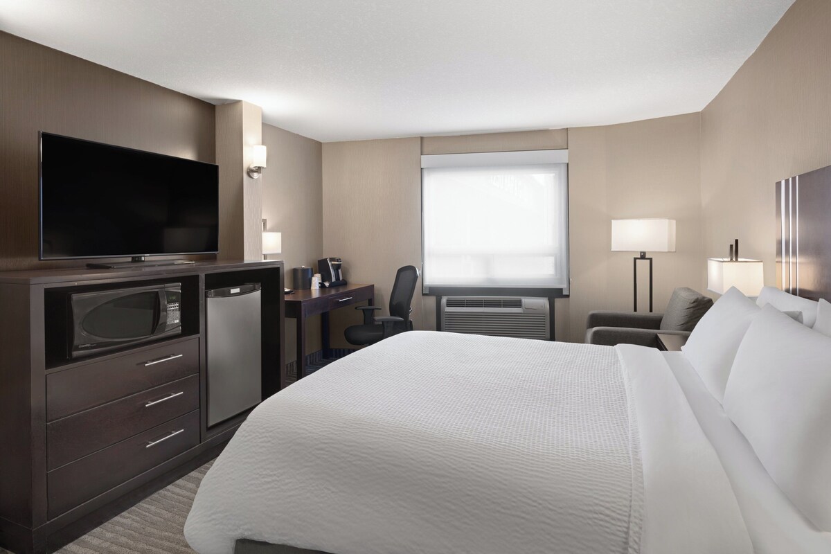 A hotel room with a bed, a desk with a computer, a TV, a microwave, a coffee maker, and a window.