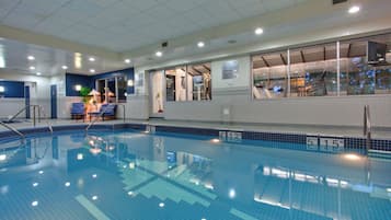 An indoor swimming pool with clear water, marked depth lines, and a sunlit area with lounge chairs.