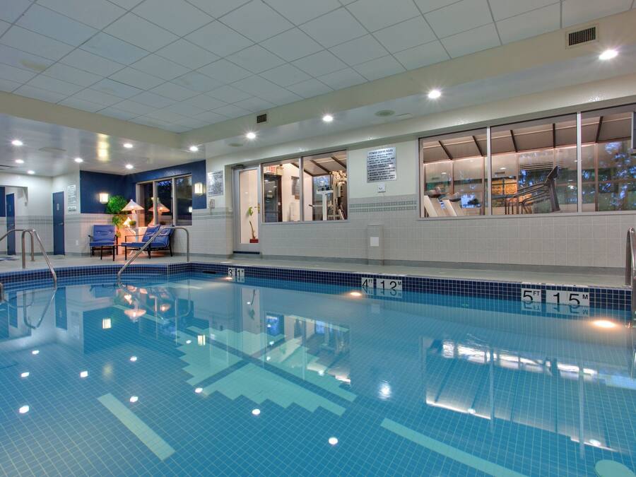 Une piscine intérieure à l’eau claire, avec des repères indiquant la profondeur et un espace ensoleillé équipé de chaises longues.