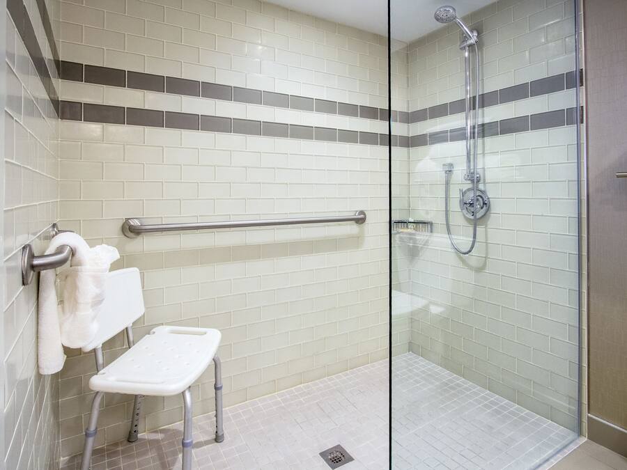 Un bagno con doccia, barra di sostegno, lavandino bianco e portasciugamani.