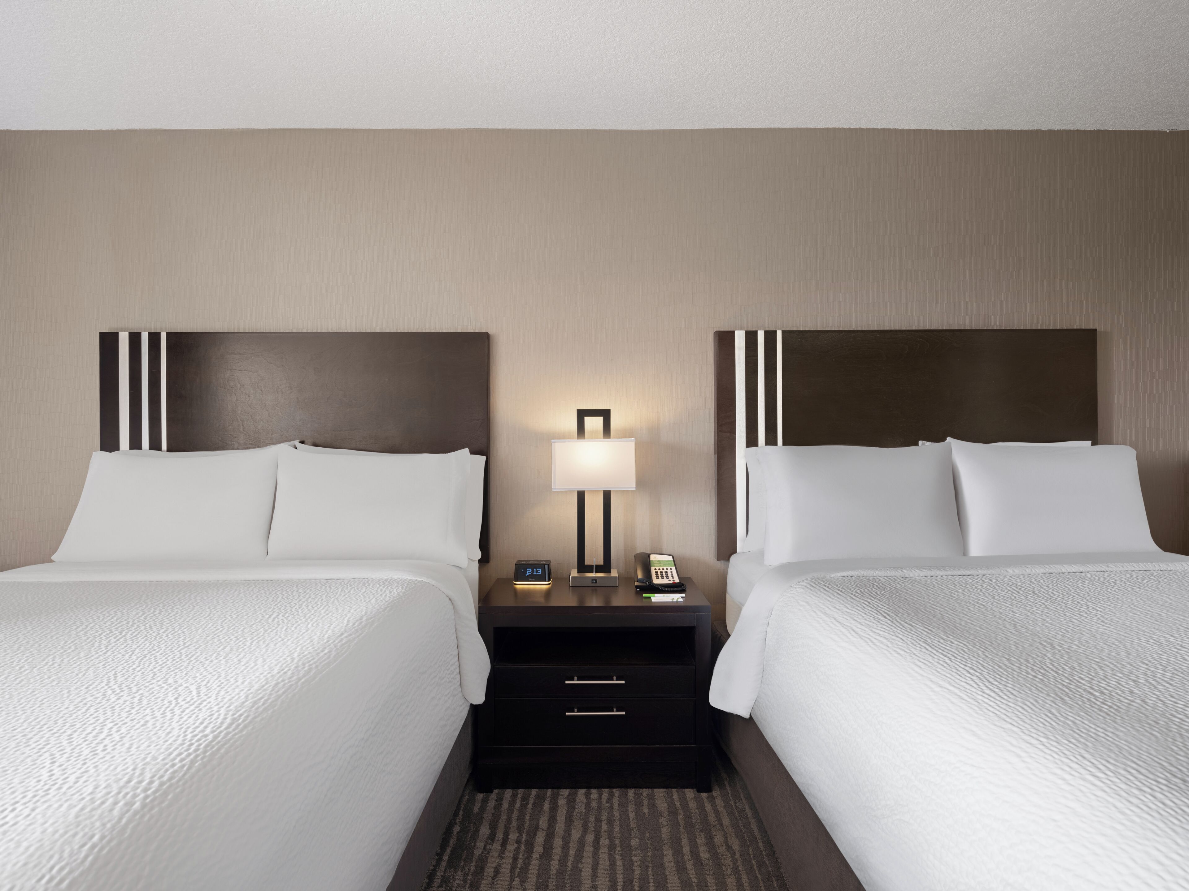 A hotel room with two beds, a nightstand with a lamp, and a phone.