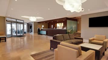 A hotel lobby with a reception desk, seating area, and a staircase leading to another floor.