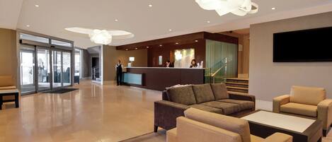 A hotel lobby with a reception desk, seating area, and a staircase leading to another floor.