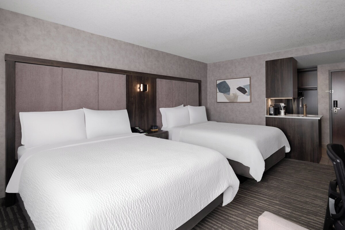 A hotel room with two beds, a small kitchenette, and a seating area.