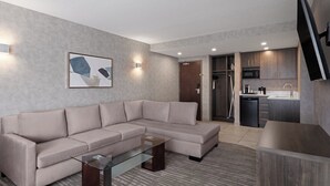 A modern living room with a sectional sofa, a glass coffee table, and a flat-screen TV mounted on the wall.