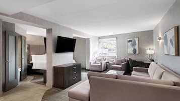 Une chambre d’hôtel moderne dotée d’un grand lit, d’un canapé, de deux fauteuils, d’un téléviseur à écran plat fixé au mur et d’un bureau avec une lampe.