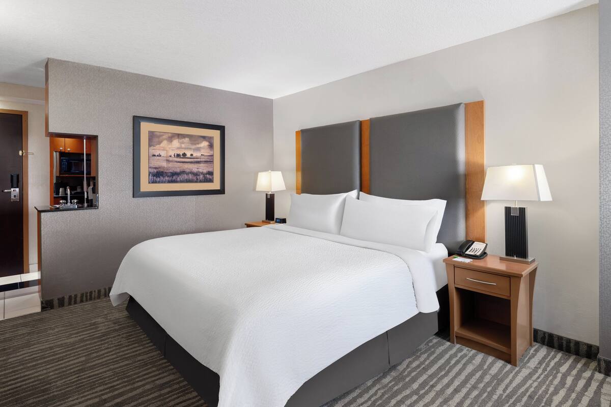 A hotel room with a large bed, two bedside tables with lamps, a framed picture on the wall, and a small desk with a phone.