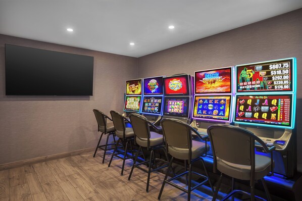 A room with multiple slot machines and a large flat-screen TV mounted on the wall.