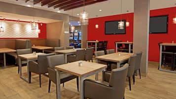 Interno di un ristorante con diversi tavoli e sedie, una parete di accento rosso e un televisore a schermo piatto montato al muro.