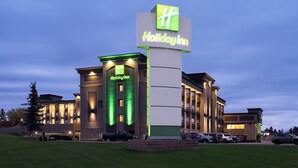 A Holiday Inn hotel with a prominent green and white logo, multiple parking spaces, and a well-lit facade.