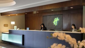 A reception desk with two staff members, a modern design with wood paneling, a neon sign, and a reception area with a counter and a digital screen.