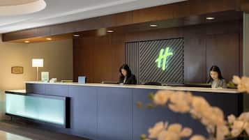 A reception desk with two staff members, a modern design with wood paneling, a neon sign, and a reception area with a counter and a digital screen.