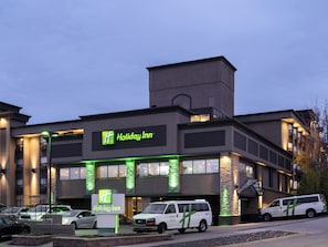 A Holiday Inn hotel with a modern design, featuring a prominent sign and a parking area with several vehicles.