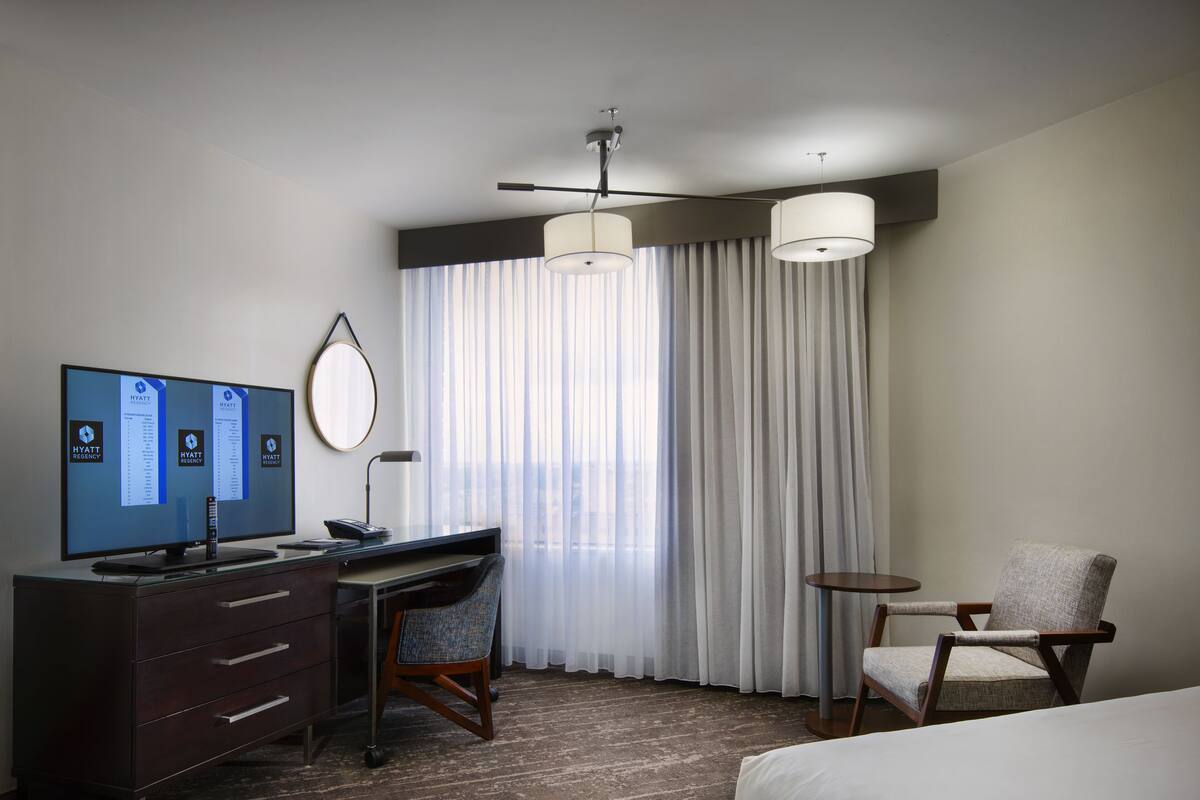 Une chambre d’hôtel équipée d’un bureau, d’une chaise, d’un lit et d’un téléviseur affichant le nom de l’hôtel.