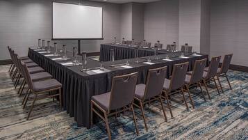 A conference room with a long table, chairs, a projector screen, and a carpeted floor.