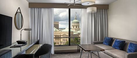 Habitación de hotel con un ventanal grande, un escritorio, un sofá y un televisor.