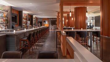 A modern bar area with a long counter, multiple bar stools, and a variety of bottles and glasses on shelves.